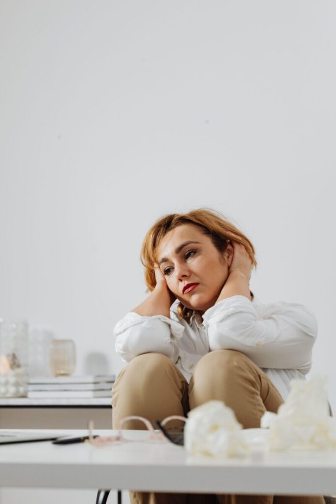 Thoughtful woman in white blouse sitting with brown pants, appearing pensive.